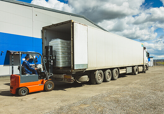 An employee drives a forklift and uses it to load pallets onto a truck for transport. 