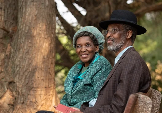An older couple sit together on a bench outdoors.