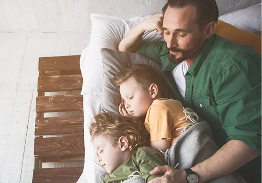 A man watches his two young children while they sleep at home. 