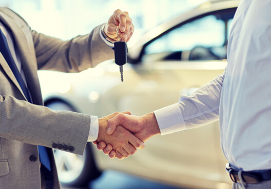 A motor dealership owner hands over the keys to a vehicle he just sold. 