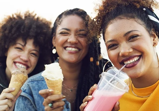 A group of young women enjoy ice-cream and milkshakes together outdoors. 