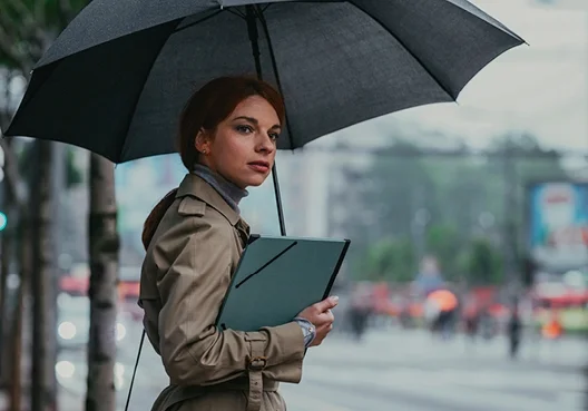 A woman shelters under a gray umbrella outside in the rain. 