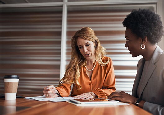 A client wearing a light gray blazer talks to her female financial adviser at an office.
