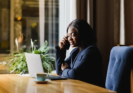 A woman sitting at her desk holding documents while talking on her cellphone