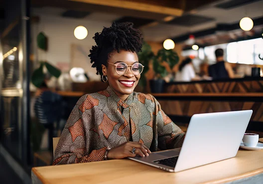 A woman wearing glasses and a printed blouse uses a laptop in a coffee shop. 