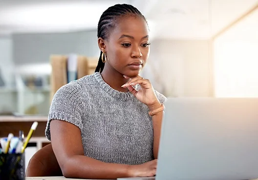 A woman wearing glasses and a printed blouse uses a laptop in a coffee shop. 