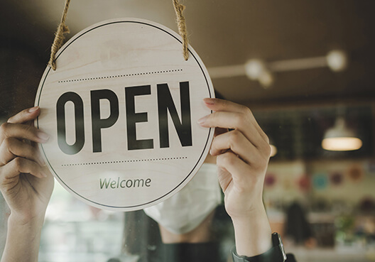 A business owner switches the sign to “open” in the window of their retail store. 