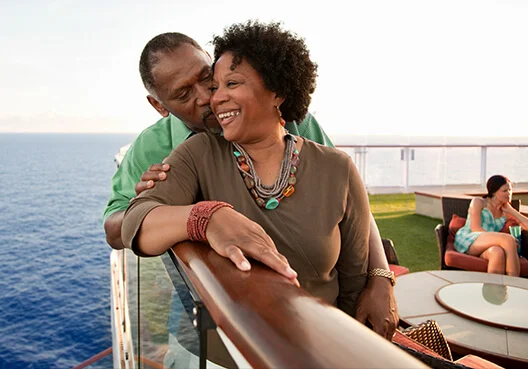 An older woman and man lean on the wooden railing of a ship’s deck while on a cruise.