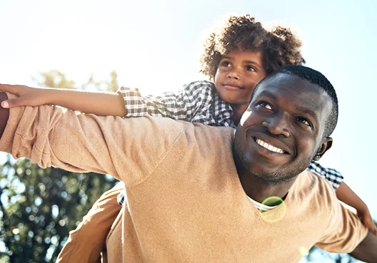 A man wearing an orange jersey plays outside with his young child.