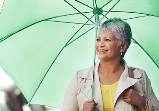 An older woman with short grey hair holds a green umbrella in one hand. 