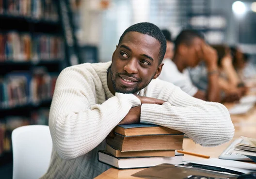 A student pursuing a career as an actuary rests his arms on a pile of library books.