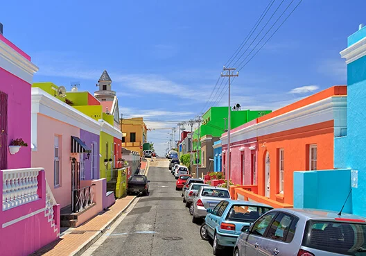 Cars parked along a vibrant street of colourful houses highlighting the need for reliable car, home & contents insurance.