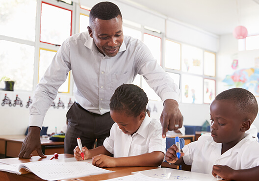 A male teacher works with young students in a classroom in South Africa. 