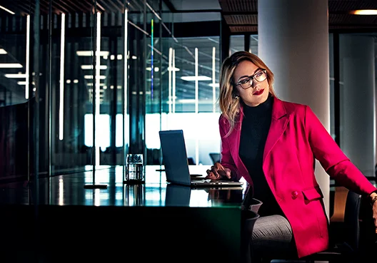 A woman in a cerise business suit at a table turning in a seat to look back