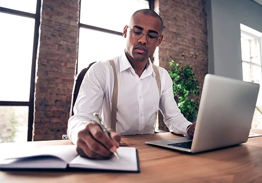 A man smiles and looks up information about debt consolidation loan on his laptop. 