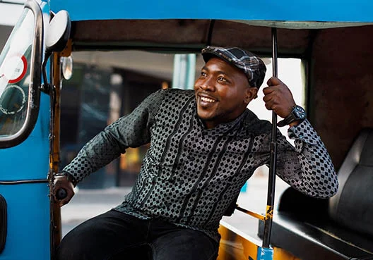 A man wearing a patterned short and cap sits in the back of a vehicle.