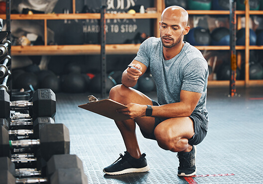 An employee squats down to check a row of weights at a fitness centre. 