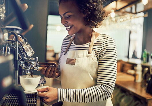 A barista wearing a cream-coloured apron prepares coffee at a café. 