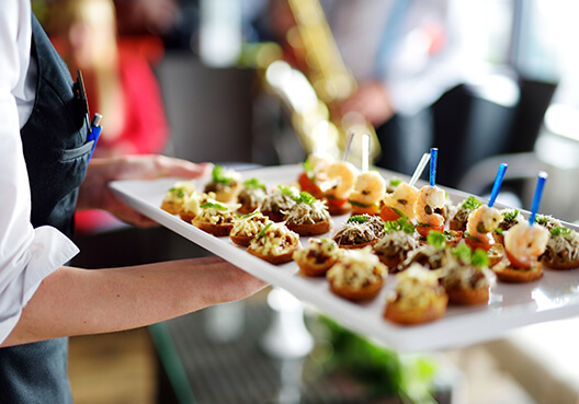 A server wearing an apron carries a tray with canapes for guests at an event. 