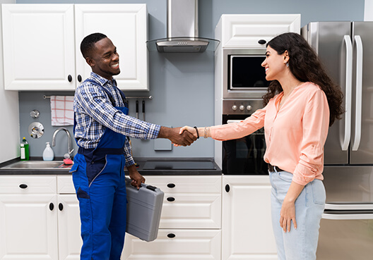A handyman carrying his tool case shakes a customer’s hand after completing a job. 