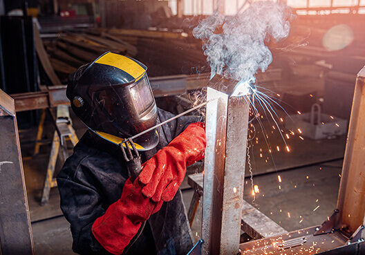A metalworker wearing full protective gear uses specialised equipment at a factory. 