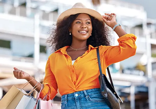 A joyful woman smiles outdoors while holding shopping bags, embodying the freedom and confidence of smart investing.