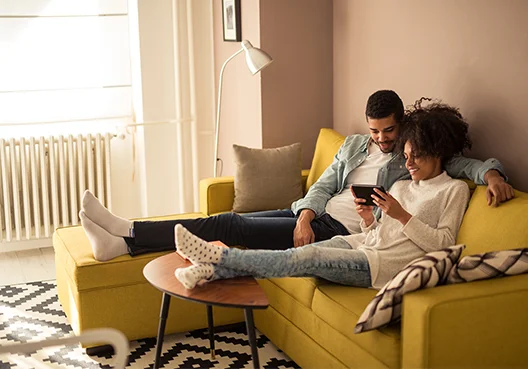 A happy couple sits on the couch of their new home, enjoying peace of mind with comprehensive home and contents insurance.