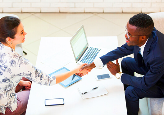 A man wearing a dark blue suit shakes hands with a woman wearing a floral blouse.