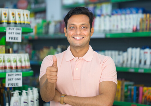 A business owner stands in front of rows of stock at his grocery store. 