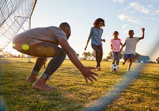 A South African couple play a game of soccer with their two children outdoors.