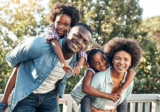 A young couple play with their children outdoors at their home.