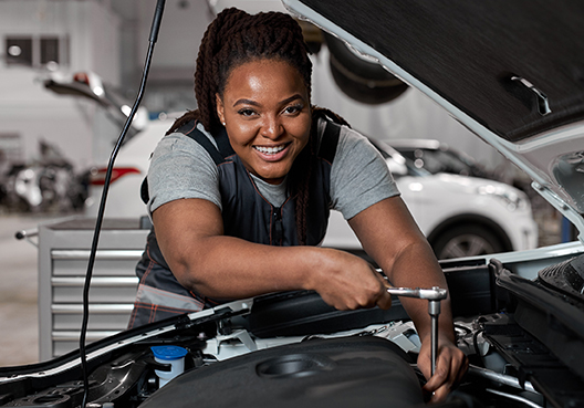 A female mechanic uses tools to fix a car’s engine at a workshop.