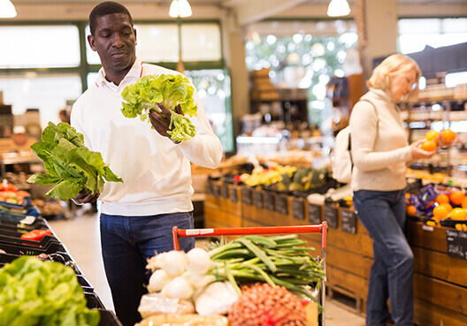 A man chooses between two heads of lettuce at a grocery store. 