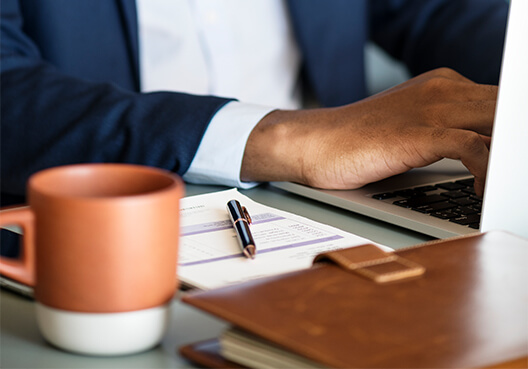 A financial adviser wearing a white shirt and dark navy blue works at a laptop.
