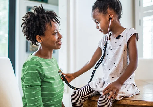 A woman wearing a green striped top lets her daughter listen to her heart with a stethoscope.