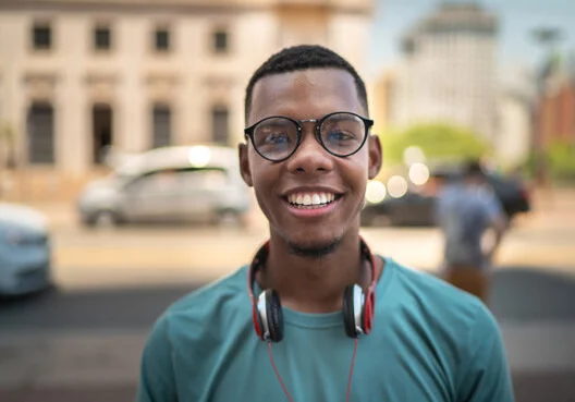 A young South African man with earphones around his neck smiles outdoors.