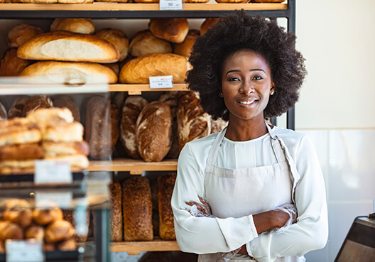 A baker with her own business stands in front of displays of fresh baked bread. 