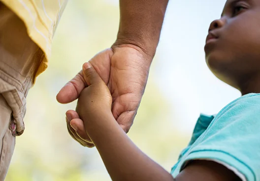 A man holds the hand of a child wearing a teal blue t-shirt. 